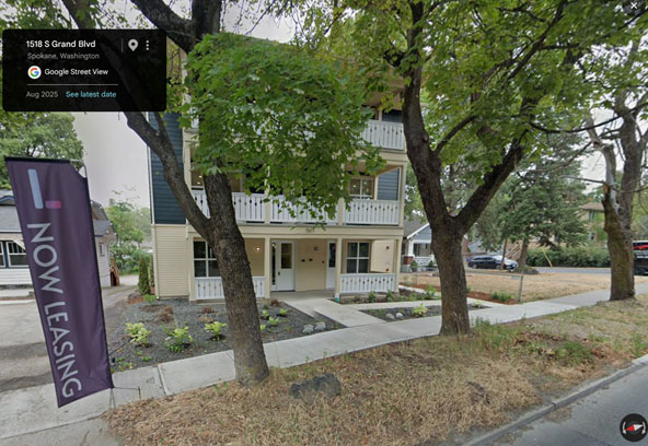 Three-story building with stacked porches and two ground-floor entrances, standing directly beside single family houses on a Spokane street